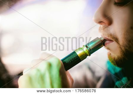 Young Vaper Man With Beard Vaping Mechanical Mod. Guy Smokes An Electronic Cigarette By Blowing A Sm