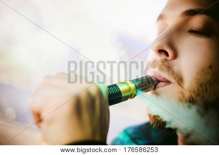 Young Vaper Man With Beard Vaping Mechanical Mod. Guy Smokes An Electronic Cigarette By Blowing A Sm