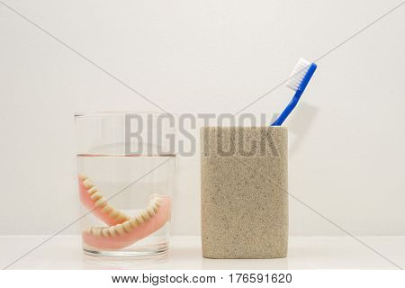 Blue toothbrush in ceramic glass, dental plates in a glass with water at the bathroom
