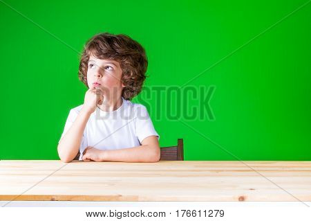 The curly-haired pretty boy stares right up sitting at a table. Close-up. Green background.