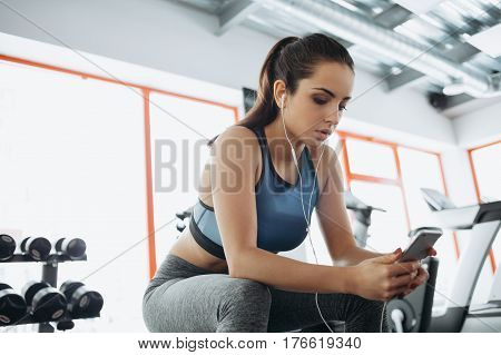 Young Woman With Earphones Listening To Music After Hard Workout In Gym.