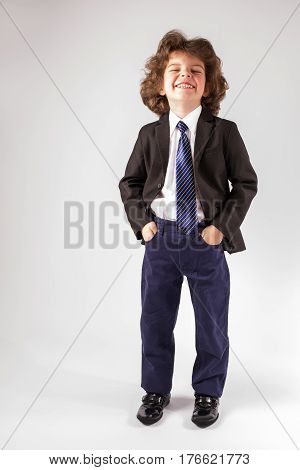 Curly cute boy is throwing back her head and laughs. Full length. Gray background.