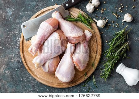 Raw uncooked chicken legs drumsticks on wooden board meat with ingredients for cooking top view