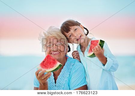 child and grandmother eating watermelon on the beach