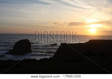 A golden setting sun inches near the crisp horizon of blue-grey ocean. A silhouetted foreground makes excellent space for a message or text to be added.