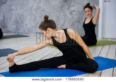 Shot of young women warming up before yoga session. Young people sitting on exercise mat in yoga class