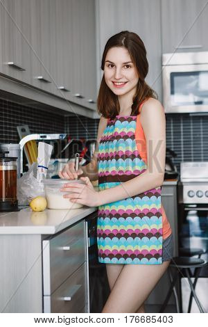 Portrait of young Caucasian woman girl with long hair cooking food pancakes standing in kitchen indoors at home authentic real people lifestyle