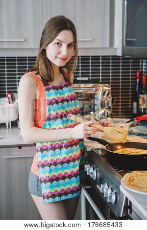 Portrait of young Caucasian woman girl with long hair cooking food pancakes standing in kitchen indoors at home authentic real people lifestyle