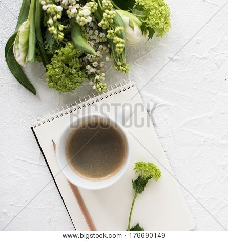Feminine flatlay with spring flowers and ccoffee on white textured tabletop