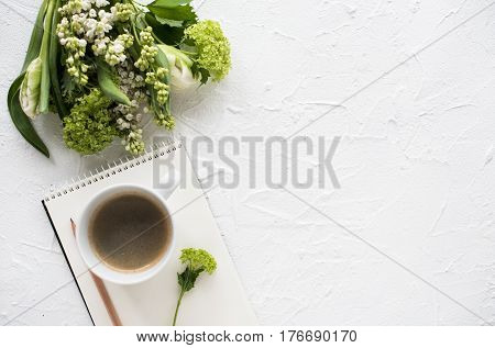 Feminine flatlay with flowers and ccoffee on white textured tabletop, design ready arrangement