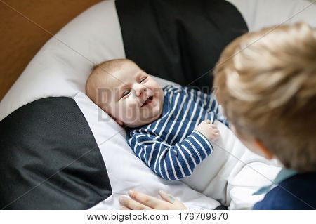 Happy little kid boy with newborn baby boy, cute brother. Siblings. Schoolchild and baby playing with colorful toys and rattles together. Kids bonding. Family of two bonding, love.