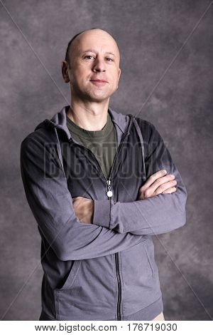 Baldheaded Man With Crossed Arms In Front Of Gray Background