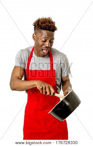 young desperate and confused black afro american man in chef apron holding cooking pot and spoon in his hands looking lost and overworked in male home cook concept isolated on white background