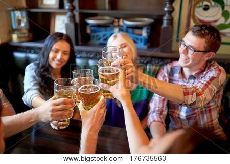 people, leisure, friendship and celebration concept - happy friends drinking draft beer and clinking glasses at bar or pub