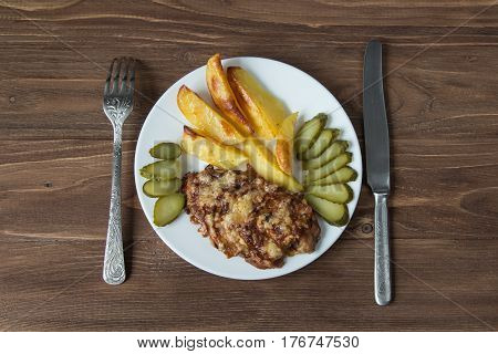 Grilled meat with potato and cucumbers on a wooden background.