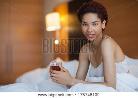 Young Happy Black Woman Sits In A Bed And Drink Tea.