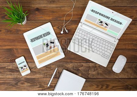 Working Place of web Designer on wood Table with responsive Site Theme on Laptop Tablet and Telephone Screens and blank Page of Paper Notepad Top View flat Lay.