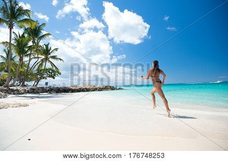 Young pretty woman with beautiful body in swimsuit running in ocean water sunny day at tropicl beach wellness concept