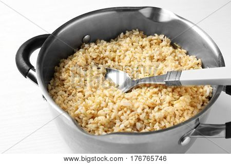 Pan with boiled brown rice on white background