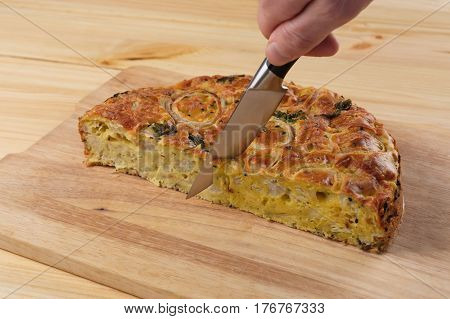 Man's hand with a knife cuts a pie kish on a wooden board