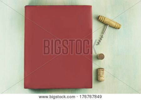 A mockup with a vibrant pink book, a corkscrew, and wine corks, shot from above on a teal background with a place for text