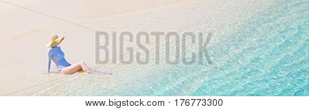 panorama view of young woman in rashguard and sunhat enjoying the perfect caribbean beach and protecting her skin from sun exposure during summer vacation copyspace on the right