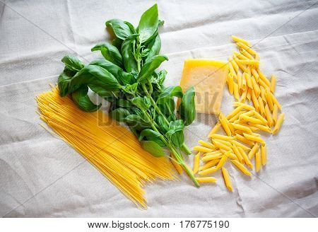 Basil parmesan raw cappellini and penne pasta on gray tablecloth