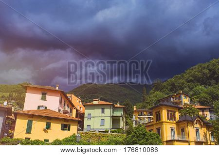 Beautiful toned cityscape of italian Varenna city with building green mountain trees and dramatic cloudy sky before the rain