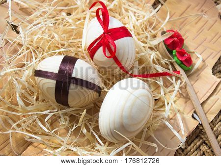 Easter eggs with ribbon and red flowers. Background birch bark and straw