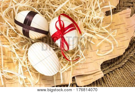 Easter eggs with ribbon and red flowers. Background birch bark and straw