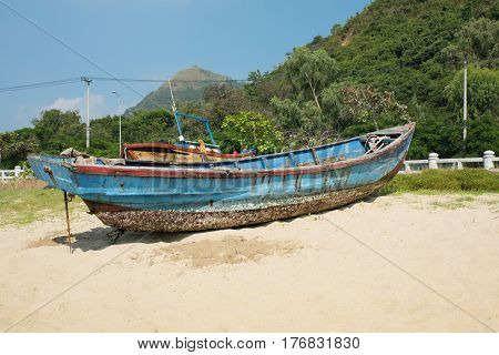 Broken yacht on the seashore. Old blue boat on the sand near the sea or the ocean