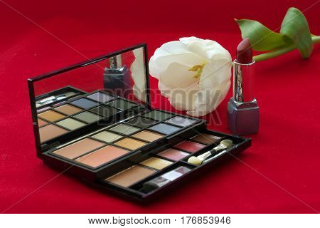 Cosmetic set lipstick eye shadow powder white tulip on red velvet background