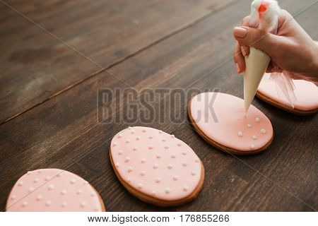 Decorating wedding sweets and desserts with icing. Pink cookies with white icing on rustic wooden empty table closeup.