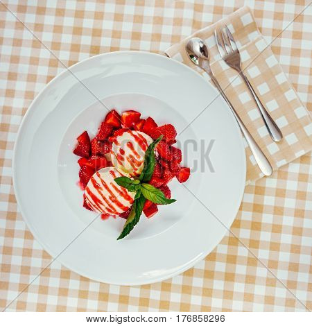 Strawberry ice cream dish with fresh strawberry and green petal serve on decorated with checkered cloth table