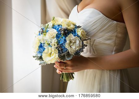 Bride holding delicate and tender marriage bouquet of yellow roses and other flowers, with green petals