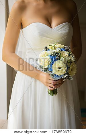 Bride holding delicate and tender marriage bouquet of yellow roses and other flowers, with green petals