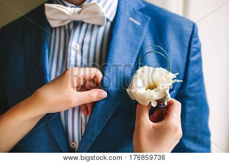 Hands adjusting yellow boutonniere pinned to a grooms blue jacket