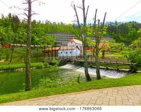 View on waterfall, mill in white building, pedestrian bridge in Park Postojna jama near Postojna Cave, famous attraction in Slovenia.