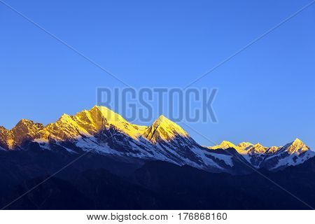Bright Morning Mountain View in Nepalese Himalaya with remote snowy peaks highlighted by rising sun while deep valley still in shadow