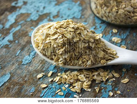 raw oatmeal is scattered on the desk of the bank in which the oat flakes are stored. blue background in the style of Shabby Chic. white spoon with uncooked oatmeal