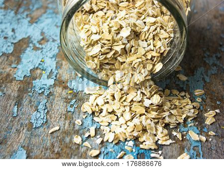 raw oatmeal is scattered on the desk of the bank in which the oat flakes are stored. blue rural background in the style of Shabby Chic. white spoon with uncooked oatmeal