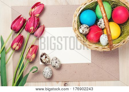Easter eggs beautiful red tulips blank note on the wooden background.