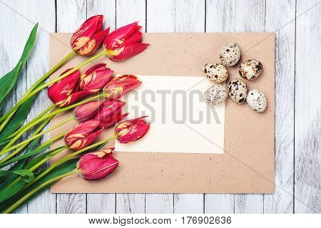 Easter eggs beautiful red tulips blank note on the wooden background.