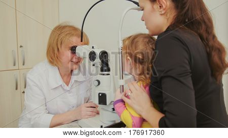Woman optometrist checks eyesight at little girl - child's ophthalmology, telephoto