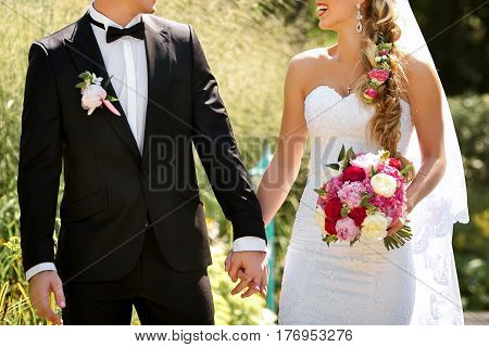 Young wedding couple hold each other on by hands and walking in park