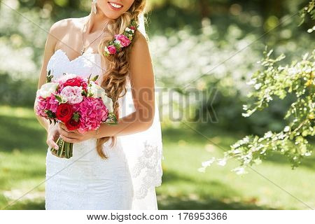 Bride holding delicate and tender marriage bouquet in white and pink colours with green petals. Beautiful sunny day in park.