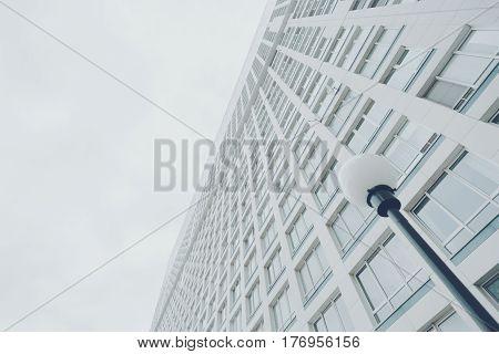 View from bottom of contemporary white and teal residential or business skyscraper building with regular structure of windows in Moscow on a bright day with round lantern in foreground