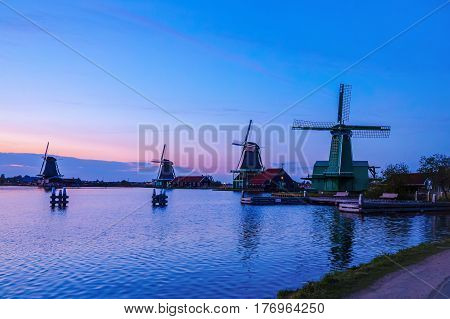 Dutch mill by evening. Sunset in landscape with mill the Netherlands. Dutch windmill at sunset at a lake. River Zaan with four windmills lined up at 'De Zaanse Schans' in Zaandam, Netherlands