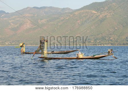 INLE LAKE, MYANMAR - DESEMBER 26, 2016: Two fishermen in traditional wooden boats to catch fish on the Inle lake