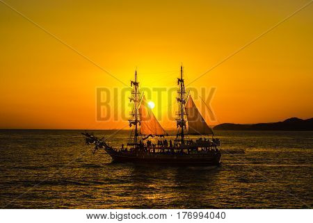 Silhouette two-masted sailing ship and of persons on Board on the background of orange sunset in the Mediterranean sea